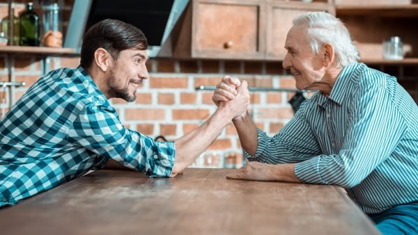 This is arm wrestling. Nice happy positive man holding his fathers hand and smiling while doing arm wrestling
